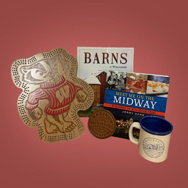 Prize Pack 2 for Member Month 2023. Bucky Badger Cribbage board, 'Barns of Wisconsin' and 'Meet Me On the Midway: A History of Wisconsin Fairs' books by Jerry Apps, a Madison leather coaster, and a Wisconsin mug with a beige exterior and Wisconsin farm in blue ink and blue interior glaze. 